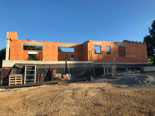 Maison en briques partiellement construite, avec échafaudages et matériaux de construction, sous un ciel bleu clair.