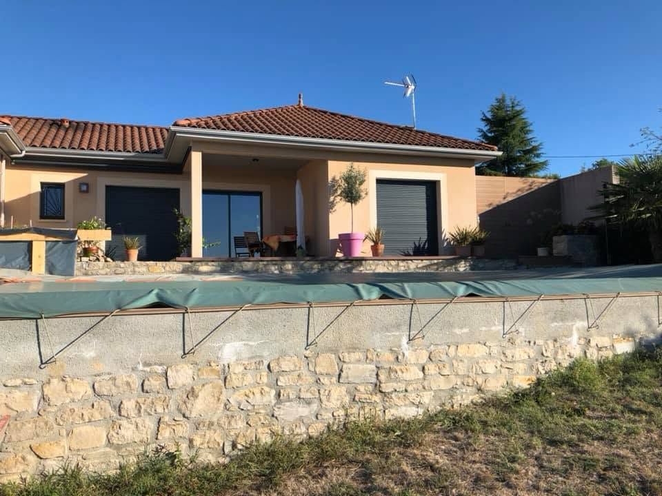 Terrasse avec piscine, mur de soutènement en pierre et maison beige au toit de tuiles rouges