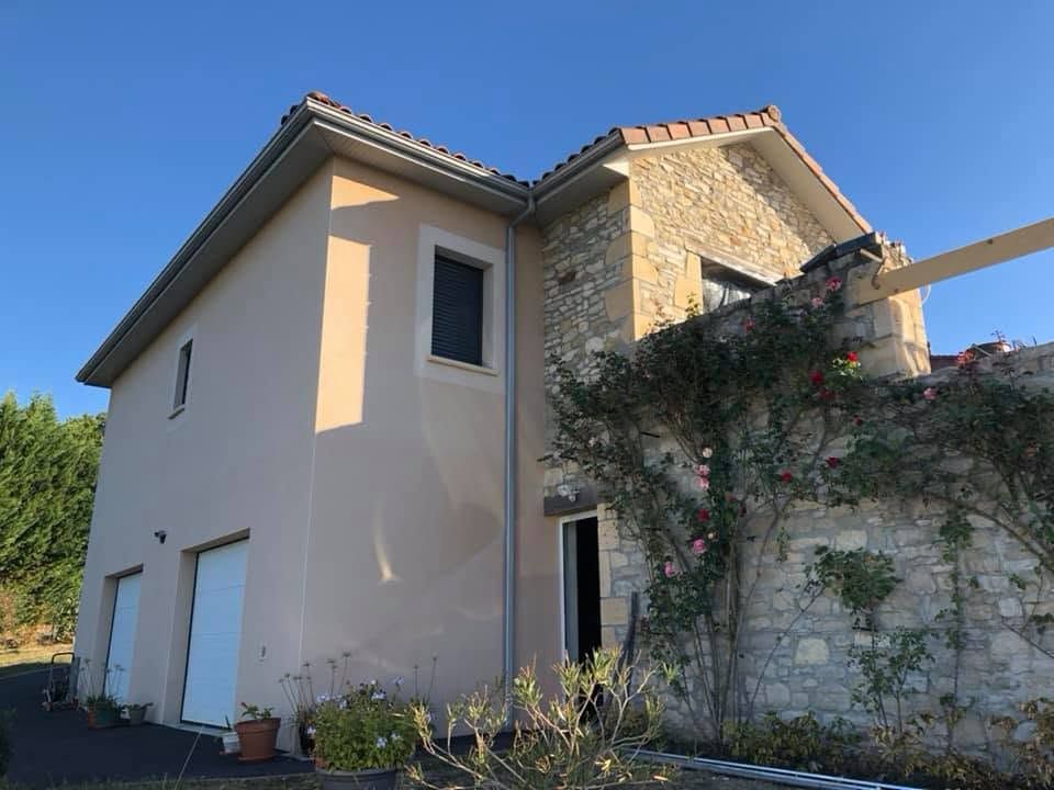 Maison beige à deux étages avec façade en pierre et toit en pente, vue de côté en plein jour