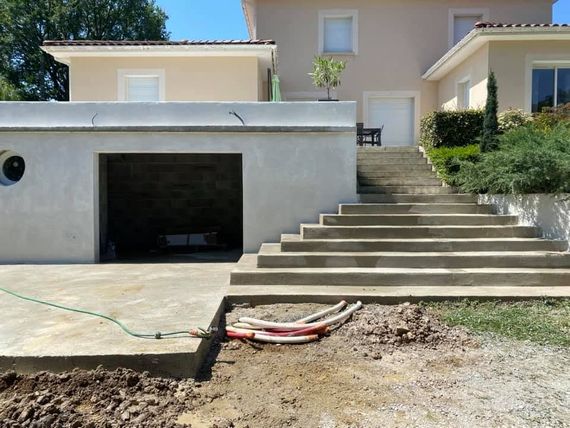 Extérieur de la maison avec garage, larges marches et cour avant en terre battue en cours d'aménagement paysager.
