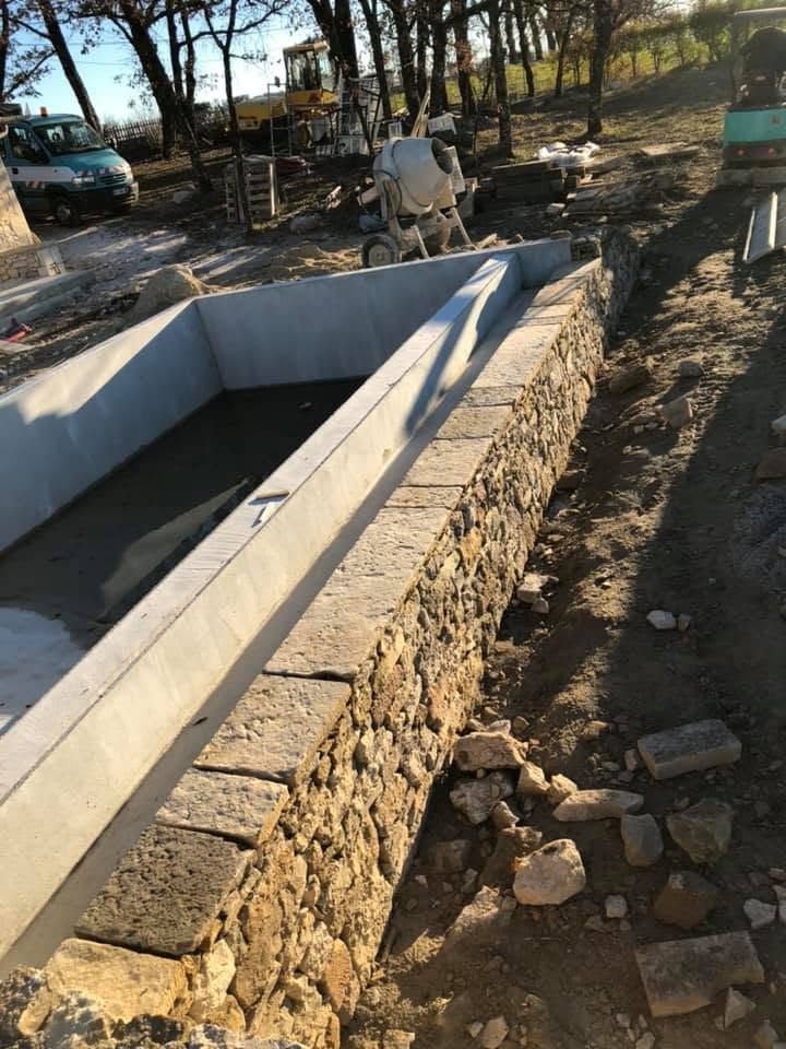 Piscine en béton avec un mur de soutènement en pierres.