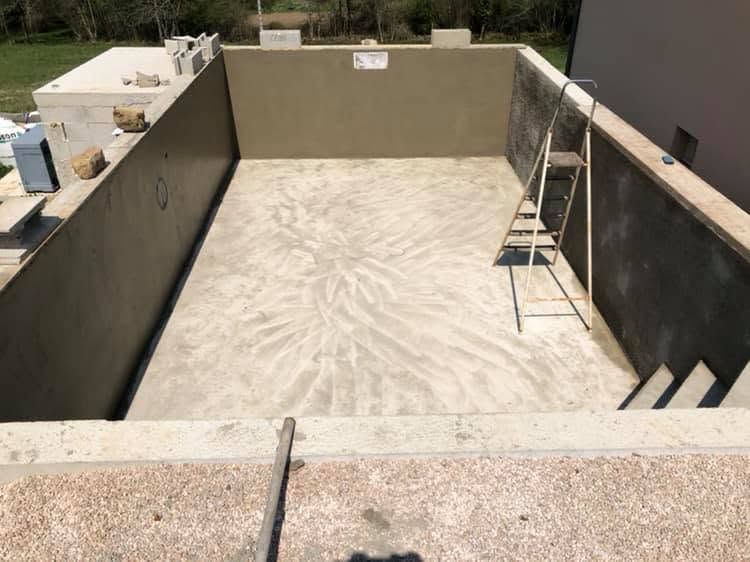 Piscine en béton vide, aux murs beiges, avec une échelle appuyée contre le mur de droite.