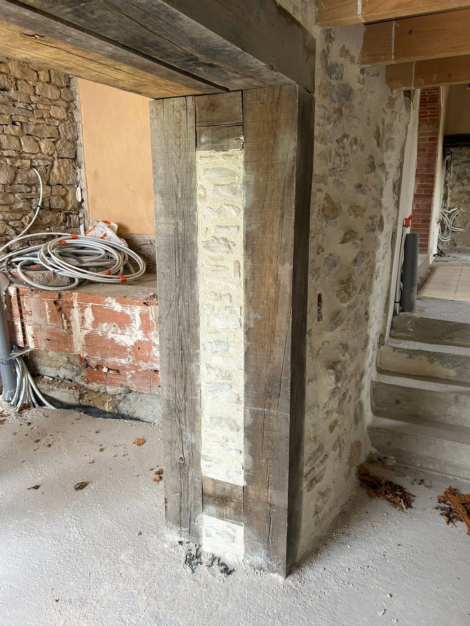 Intérieur inachevé avec un encadrement de porte en bois et en pierre, câblage apparent et escalier sur un chantier de construction