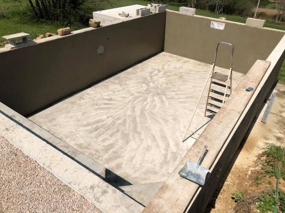 Piscine en béton vide en construction, avec une échelle et des parois beiges.