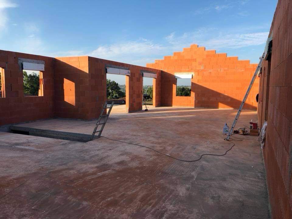 Intérieur d'un bâtiment en briques inachevé, avec des ouvertures de fenêtres et de portes ouvertes.