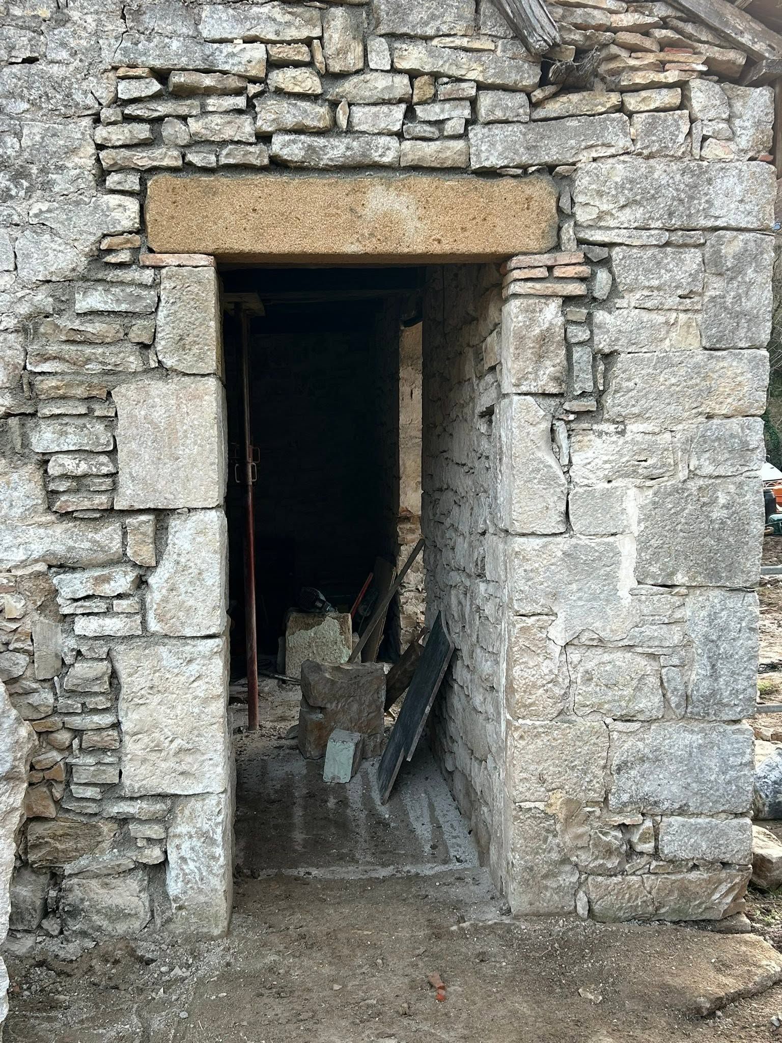 Porte en pierre dans un mur de maçonnerie brute, donnant sur un intérieur sombre.