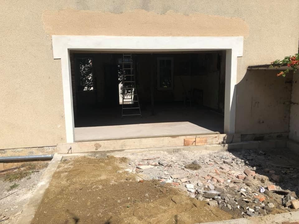 Entrée d'une maison partiellement finie avec une grande porte ouverte et des débris de construction devant