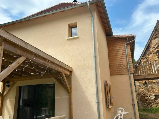 Maison beige avec toit de tuiles rouges et porche couvert dans une cour rustique