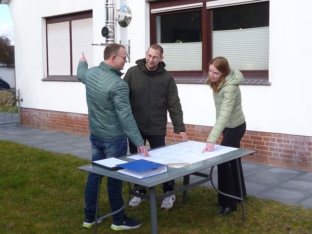 Drei Personen stehen um einen Tisch herum und schauen sich eine Karte an.