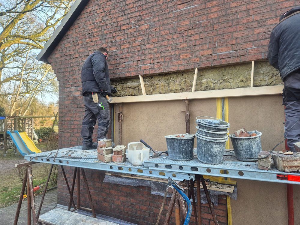 Ein Mann steht auf einem Gerüst vor einem Backsteingebäude.