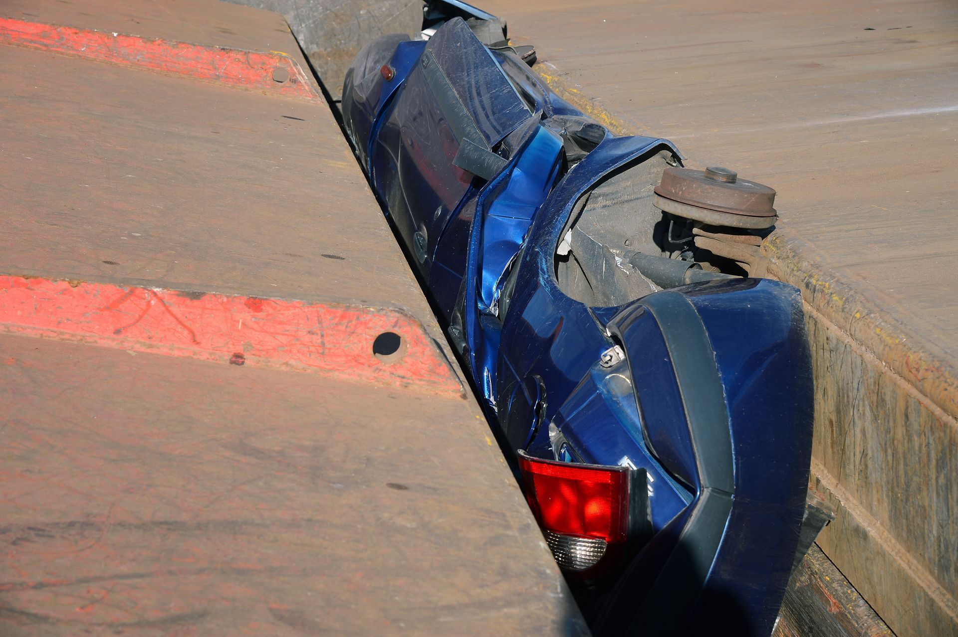 Une voiture bleue accidentée, couchée sur le flanc à côté d'un trottoir en béton avec des lignes peintes en orange.