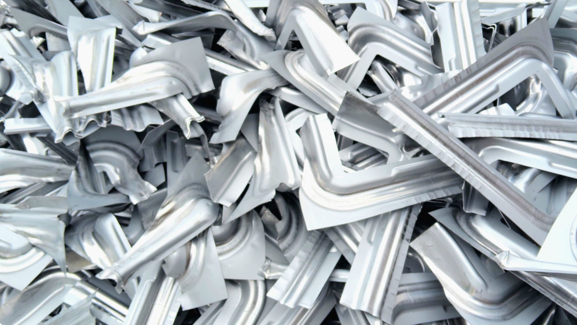 Un tas de morceaux de tôle grise industrielle en forme de L, mis au rebut et portant des motifs estampés.