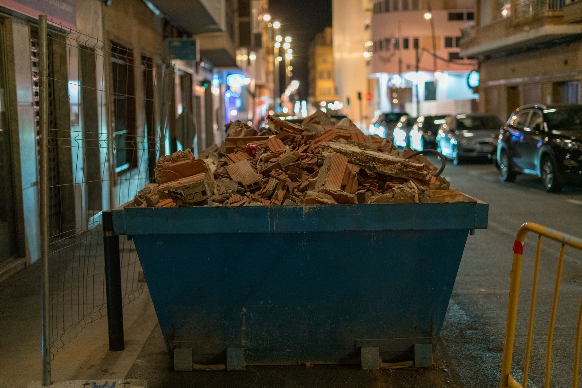 Une benne à ordures bleue de chantier, remplie de débris de briques cassées, était stationnée dans une rue de la ville, la nuit.