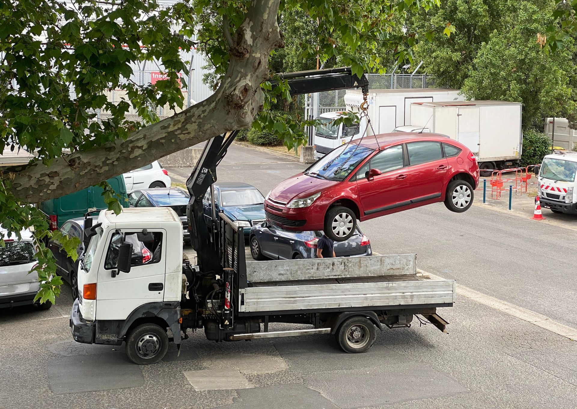 Un camion plateau équipé d'une grue hydraulique soulève une voiture rouge sur un parking.