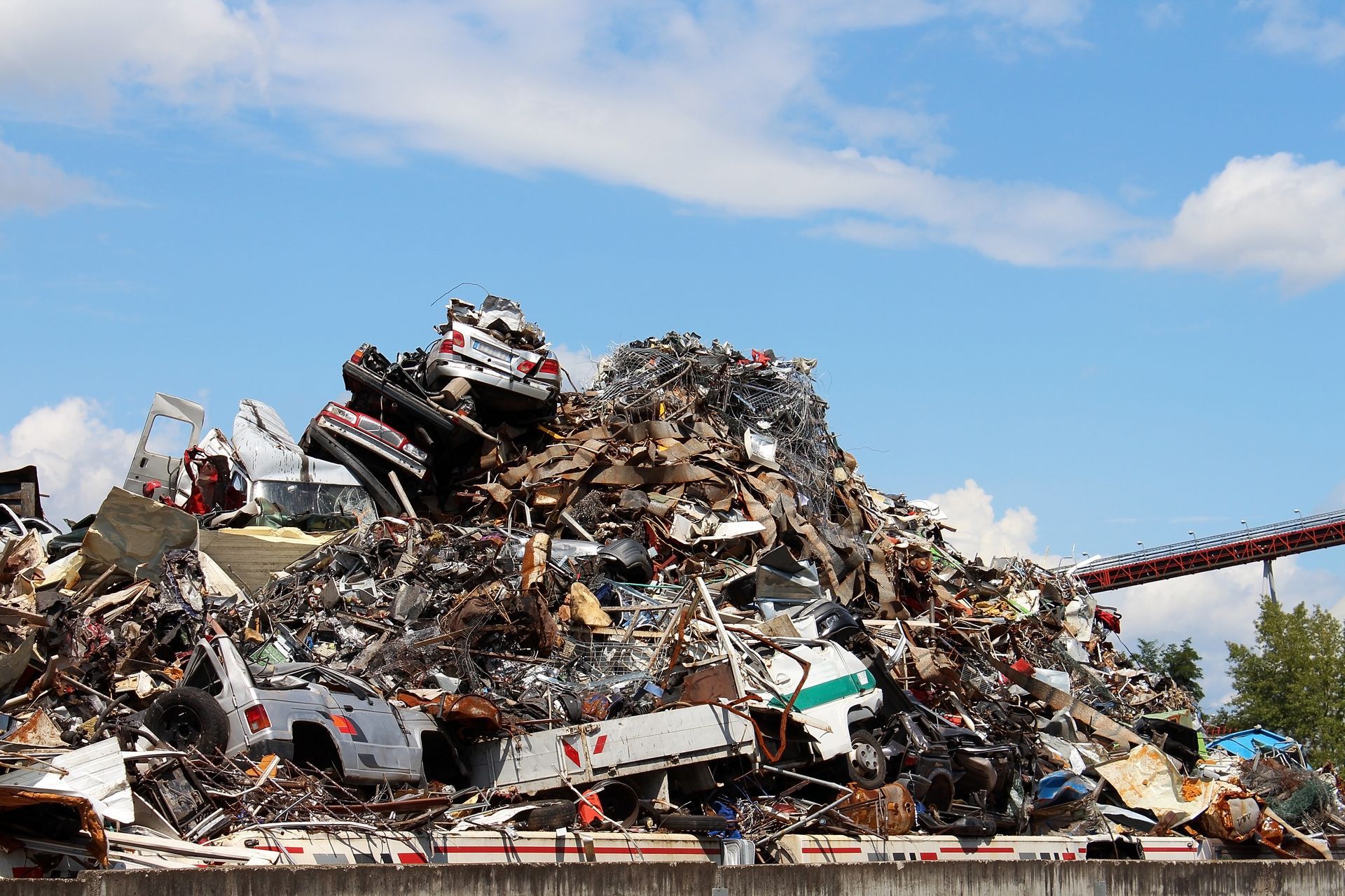 Un grand amas chaotique de voitures écrasées et de ferraille se détachant sur un ciel bleu parsemé de nuages ​​blancs.