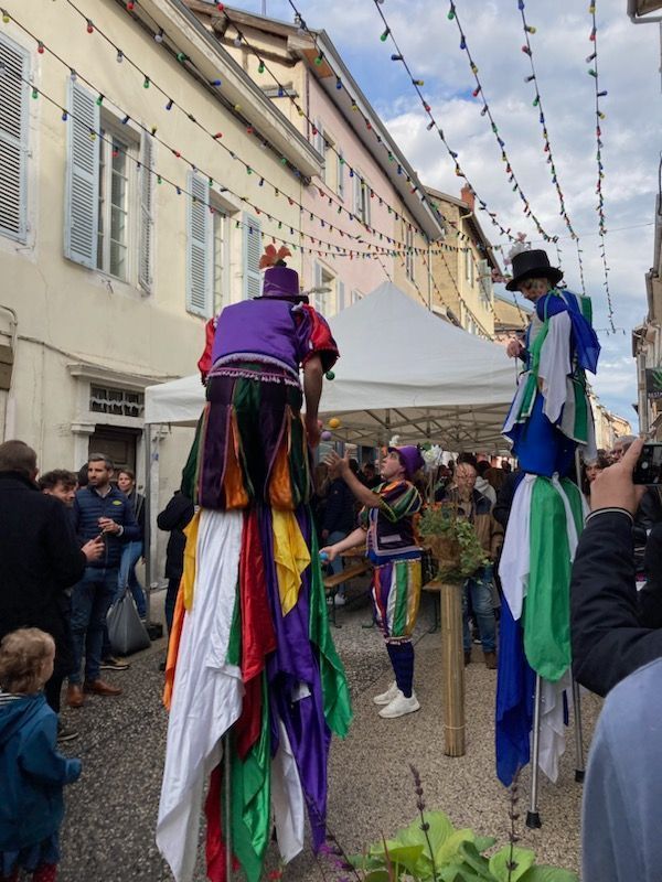 Jongleurs et échassiers déambulant dans une rue avec spectateurs