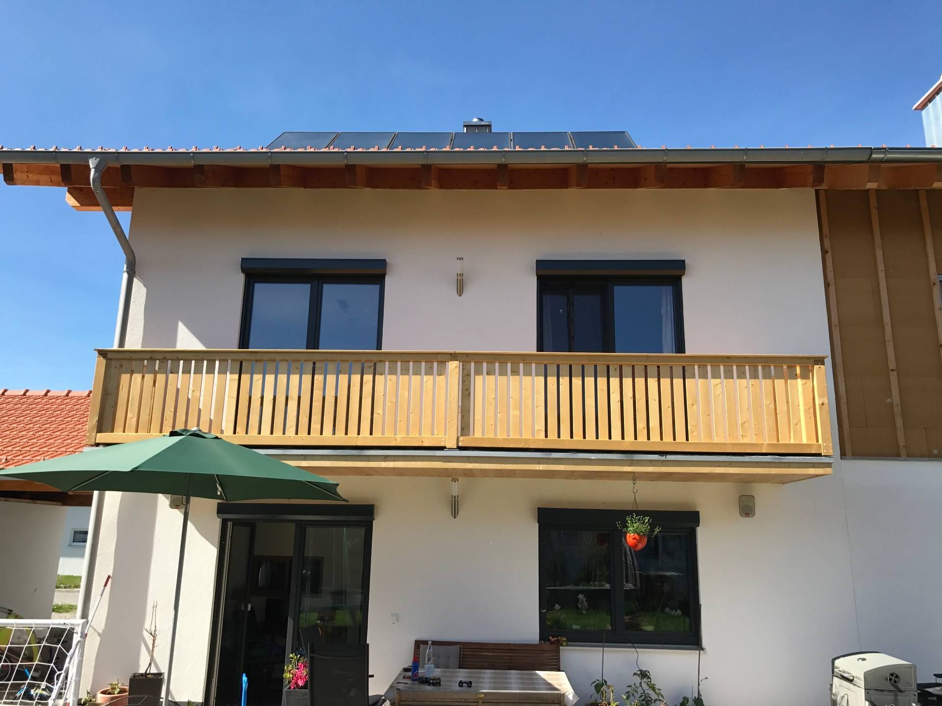 ein weißes Haus mit einem Holzbalkon und Sonnenkollektoren auf dem Dach