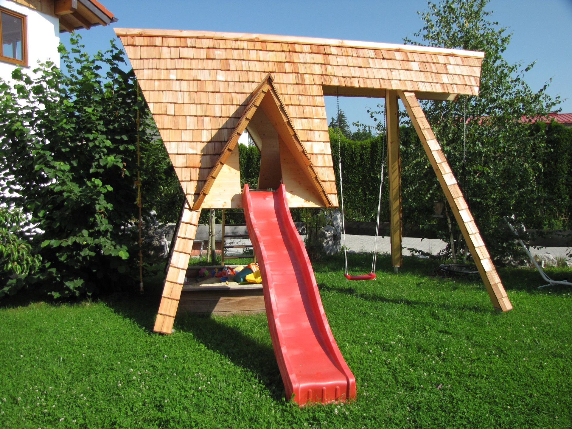 ein Holzspielplatz mit einer roten Rutsche und Schaukeln