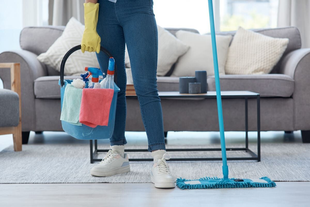 Una mujer está limpiando una sala de estar con un trapeador y un balde de productos de limpieza.