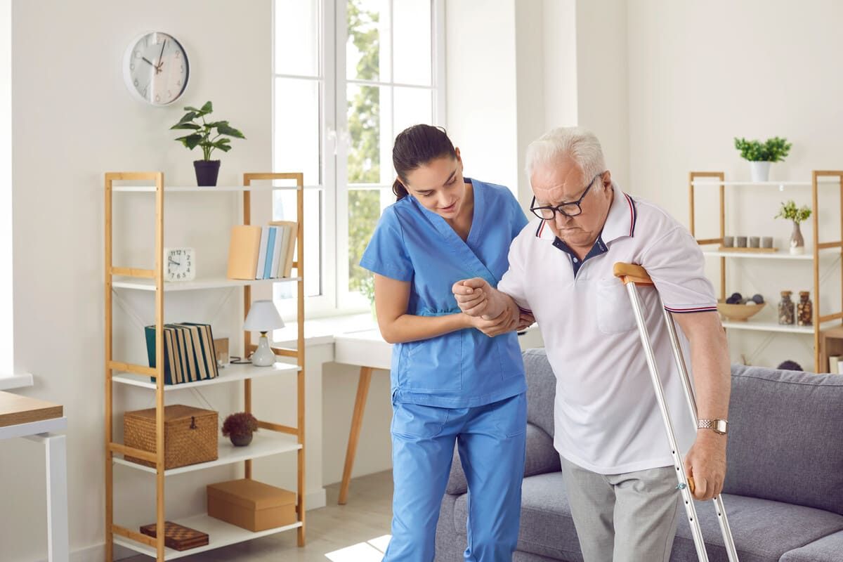 Una enfermera está ayudando a un anciano a caminar con muletas en una sala de estar.