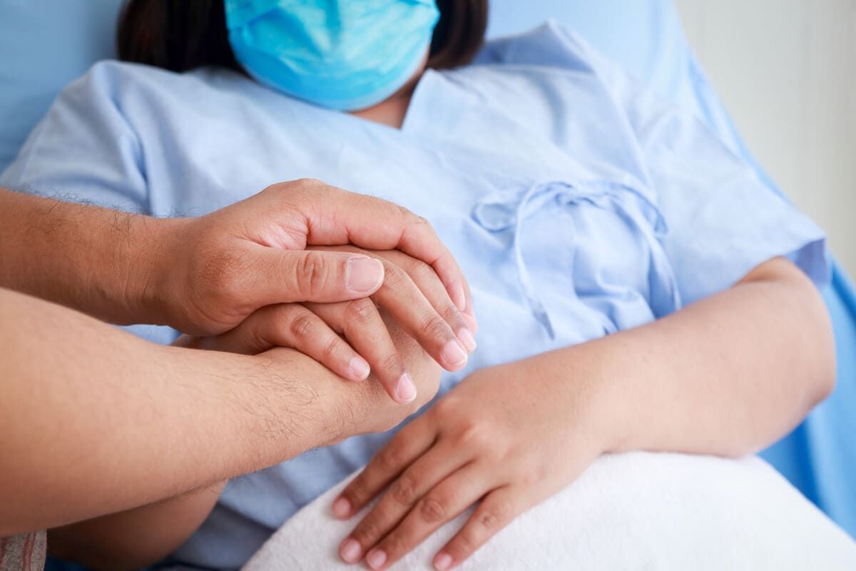 Una persona sostiene la mano de una mujer en una cama de hospital.