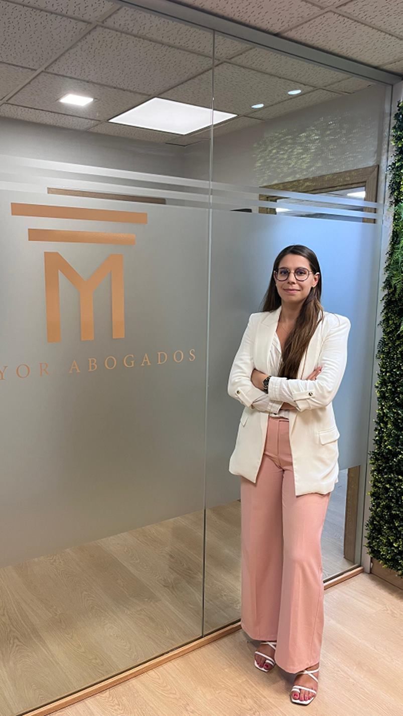 Una mujer con una chaqueta blanca y pantalones rosas está parada frente a una pared de vidrio.