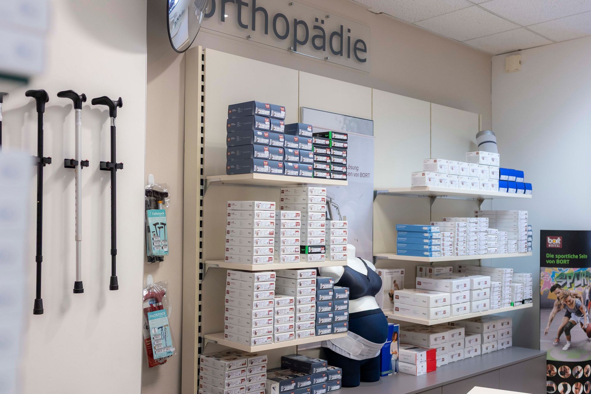 Orthopädische Produkte werden in den Regalen eines Ladens ausgestellt; links Gehstöcke, Pakete und Schachteln.