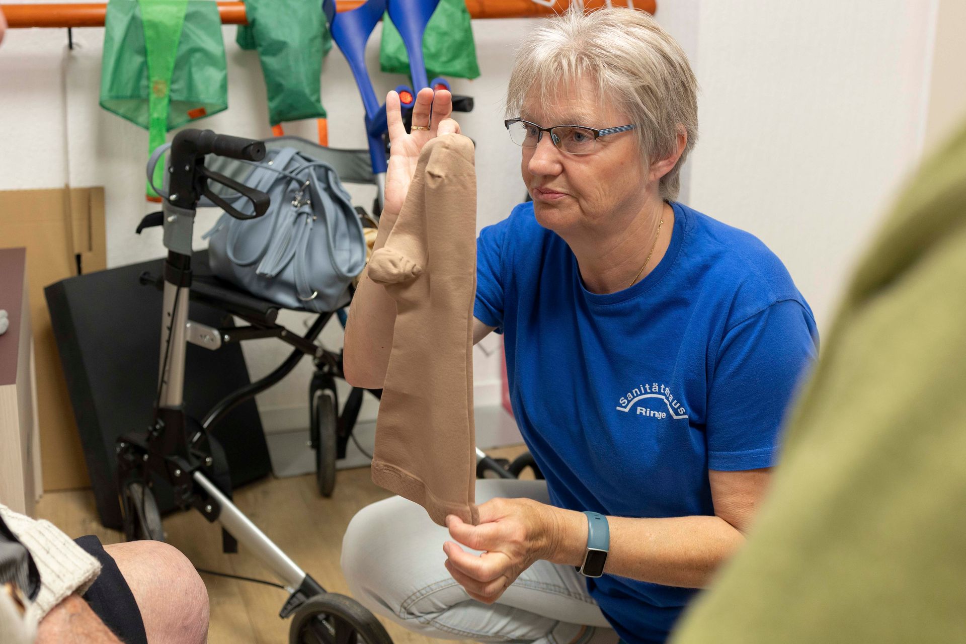Frau im blauen Hemd hält in einem Therapieraum eine Beinprothese mit Gehhilfe.