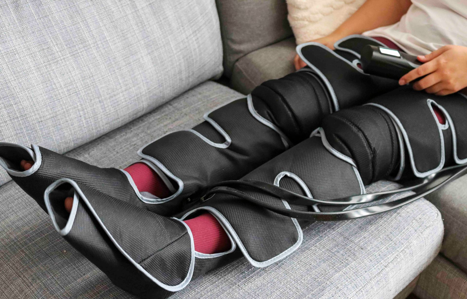 Person, die ein schwarz-graues Beinmassagegerät auf einem grauen Sofa verwendet.