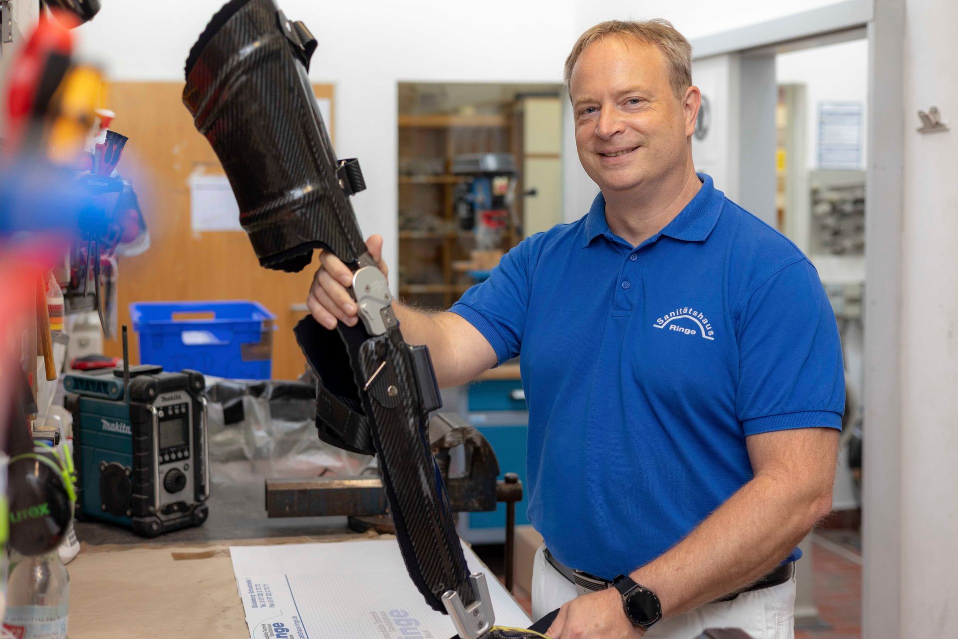 Mann im blauen Hemd hält in einer Werkstatt eine Beinprothese.