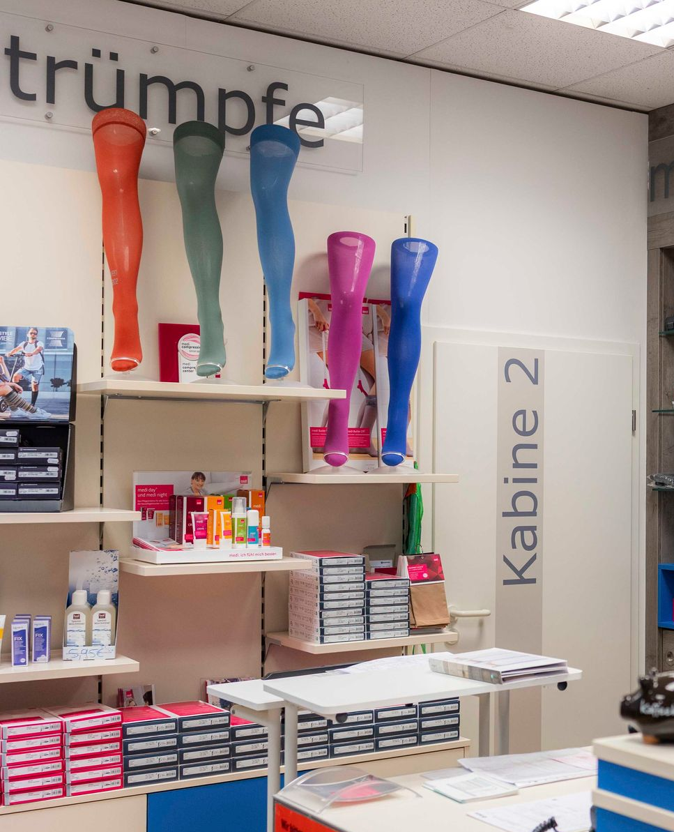 Ausstellung bunter Strümpfe auf Schaufensterpuppen in einem Geschäft mit Regalen voller ähnlicher Produkte.