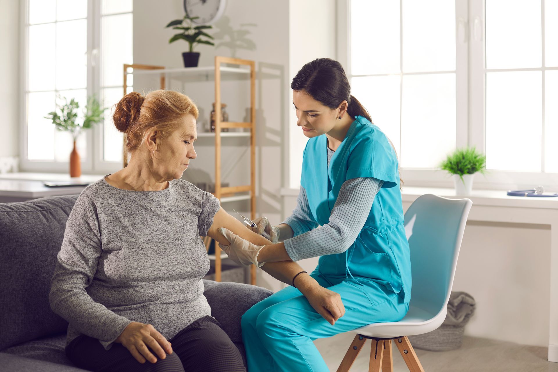 Une infirmière examine le bras d'une femme âgée dans un salon bien éclairé. Toutes deux sont concentrées.