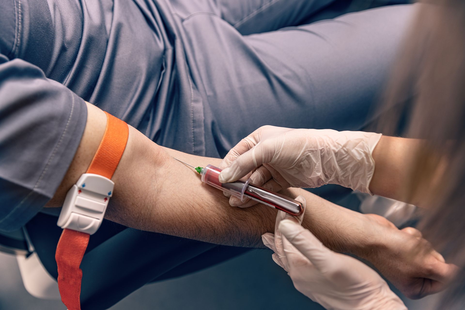 Une personne reçoit un échantillon de sang au bras, avec un garrot. Un professionnel de santé prélève du sang à l'aide d'une seringue.