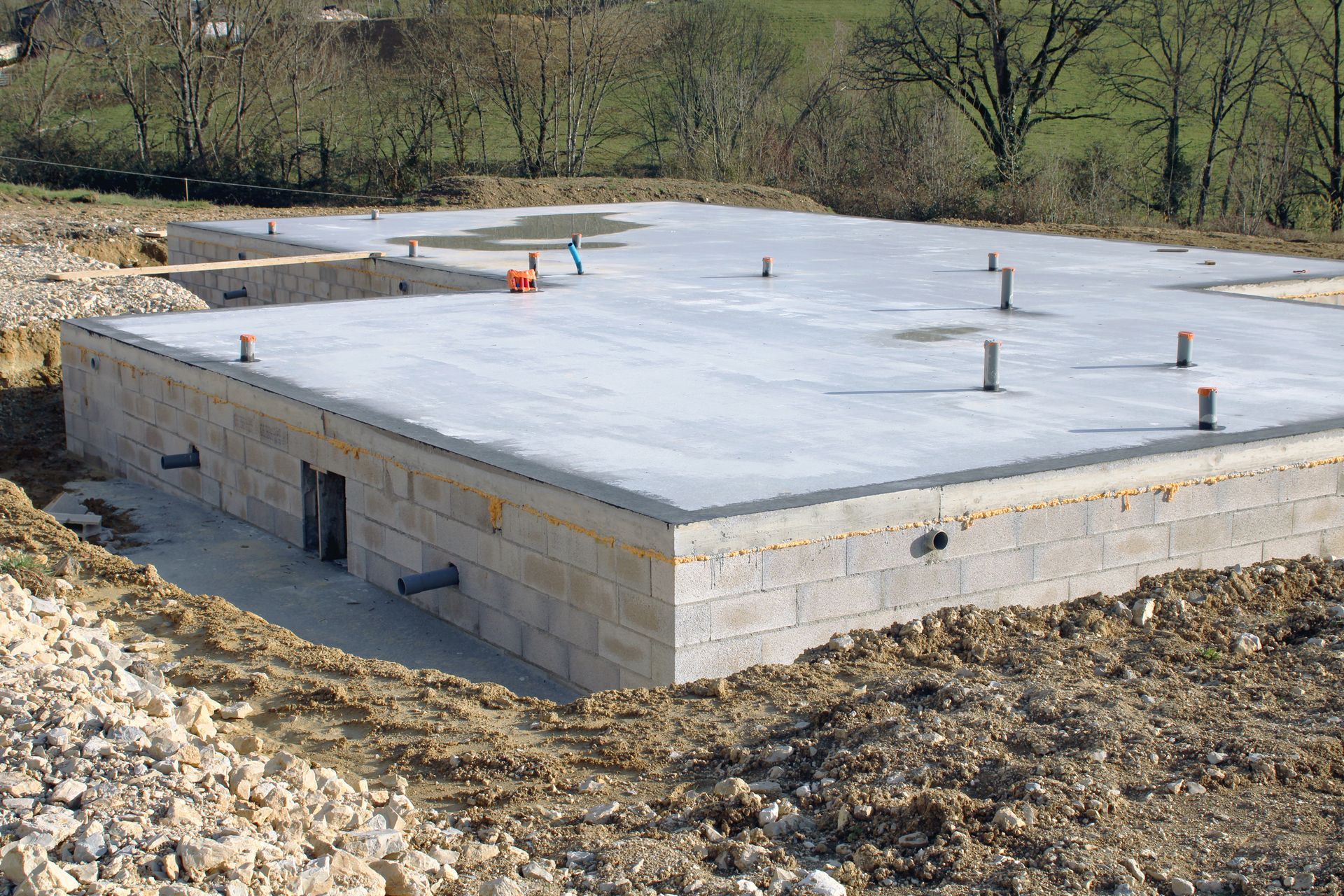 Dalle de fondation en béton sur un chantier de construction, avec plusieurs tuyaux qui en dépassent.