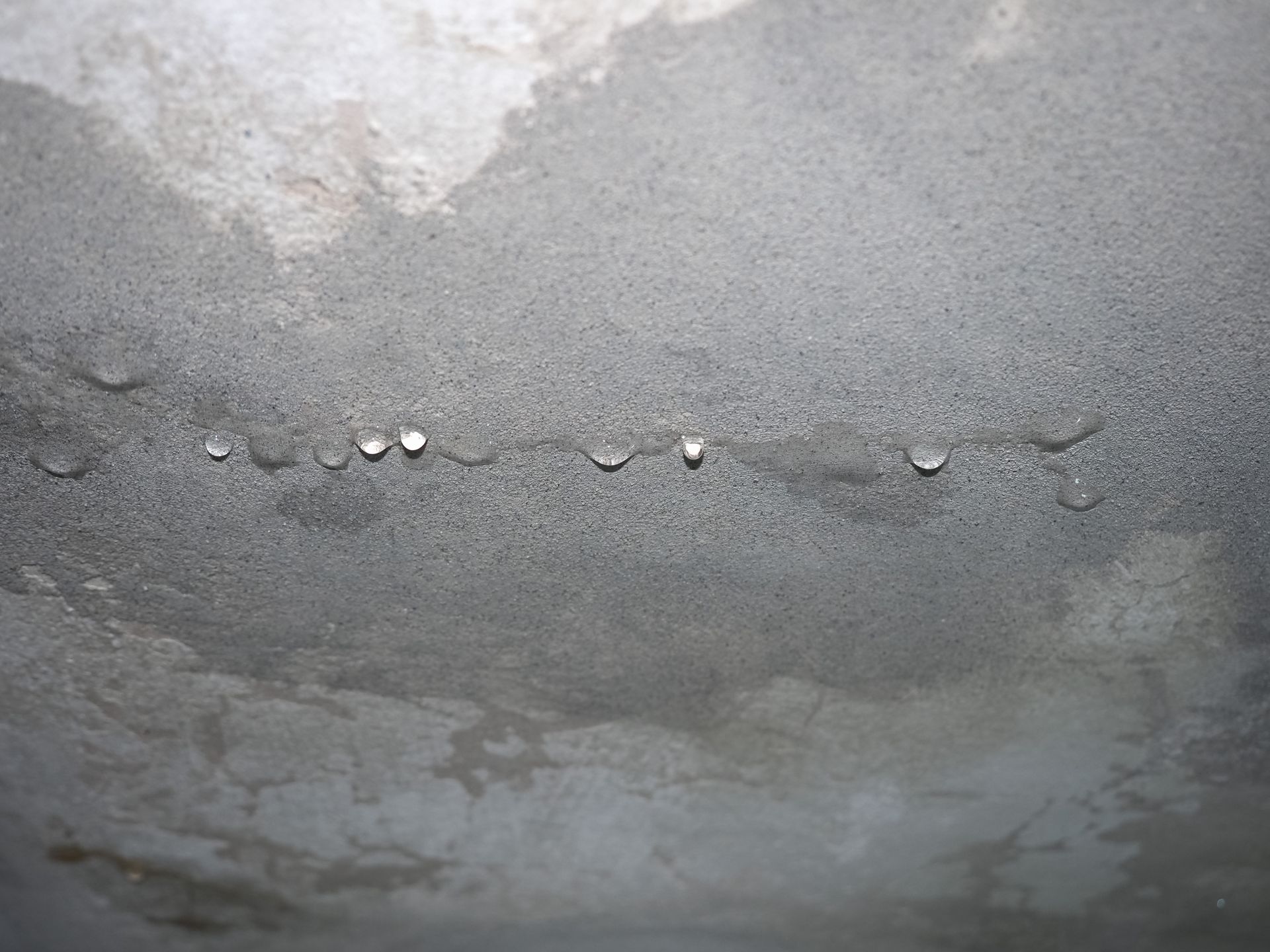 Mur en béton gris avec une fissure horizontale et de petites gouttelettes d'eau le long du joint.