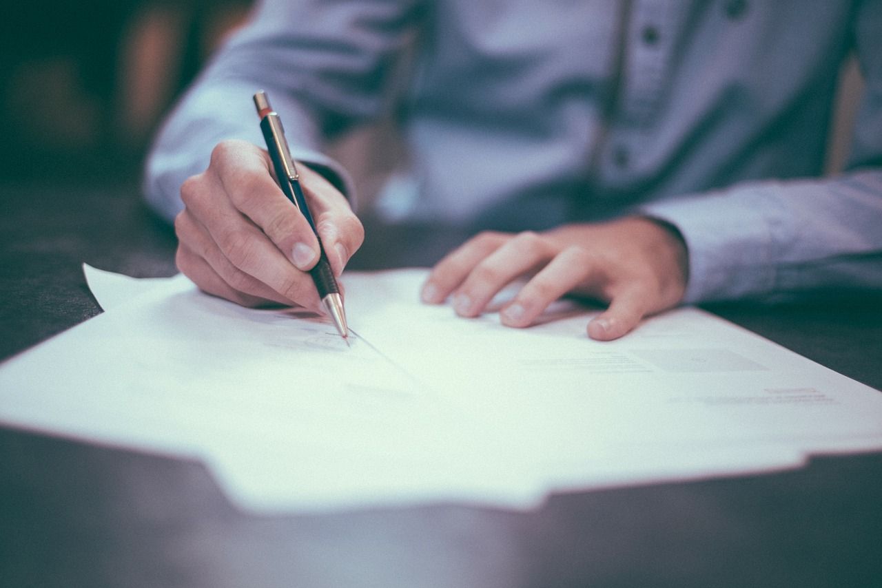 Des mains écrivent sur une feuille de papier blanc à un bureau avec un stylo