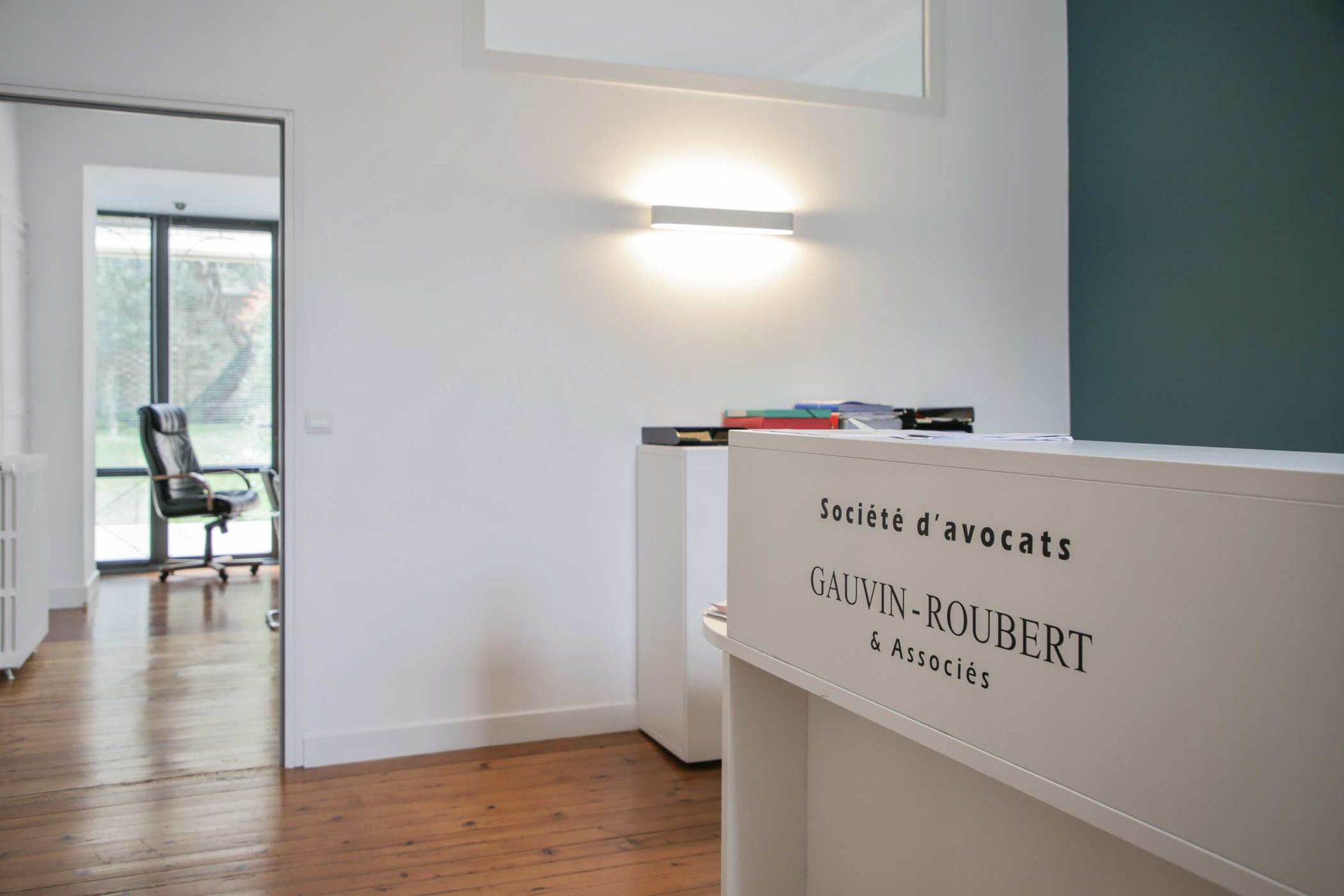 Intérieur de bureau minimaliste avec murs blancs, parquet, chaise près d'une fenêtre et comptoir au premier plan.