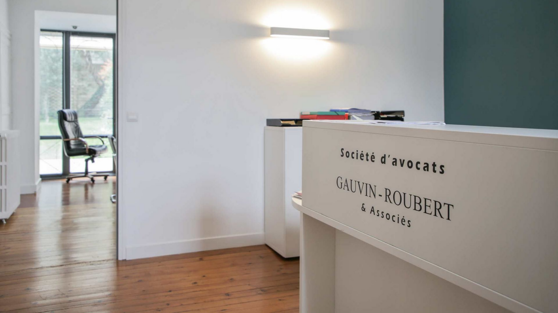 Bureau moderne et minimaliste avec parquet, murs blancs, bureau et chaise près d'une fenêtre lumineuse.