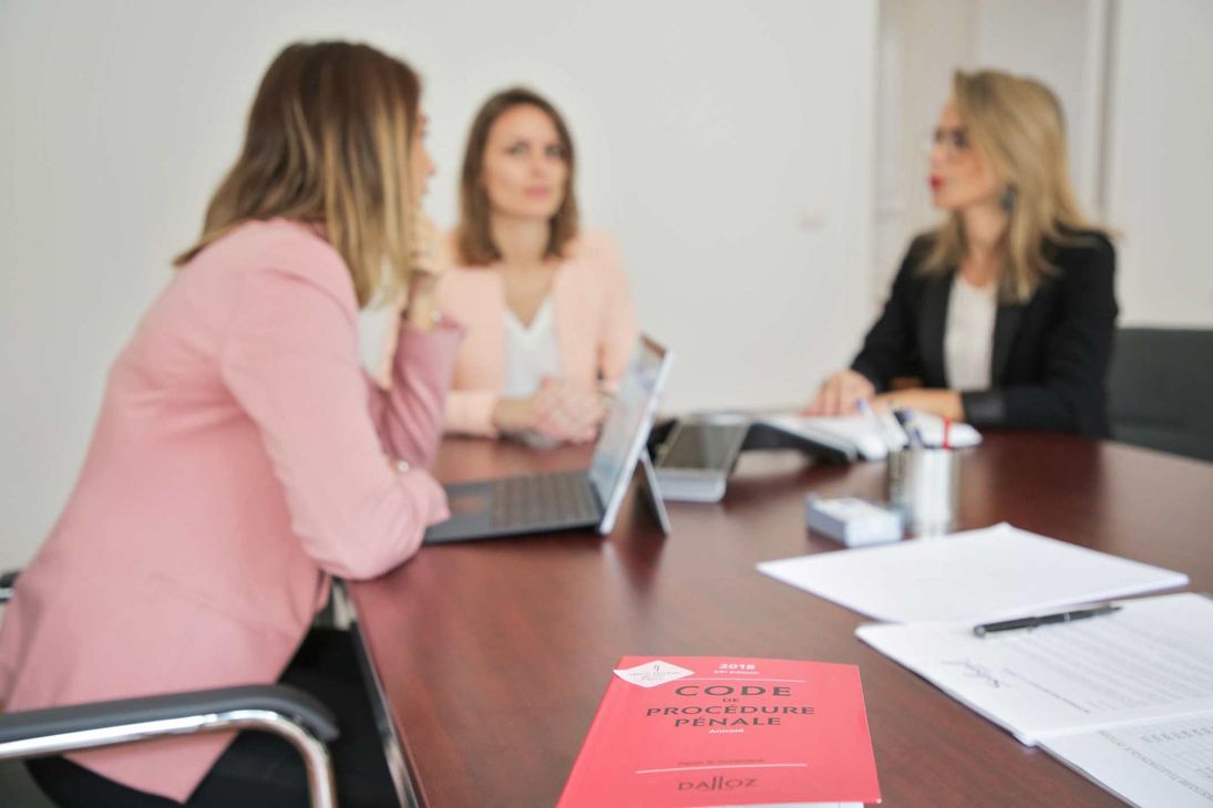 Trois personnes en réunion d'affaires autour d'une table de conférence, avec des ordinateurs portables et des documents.