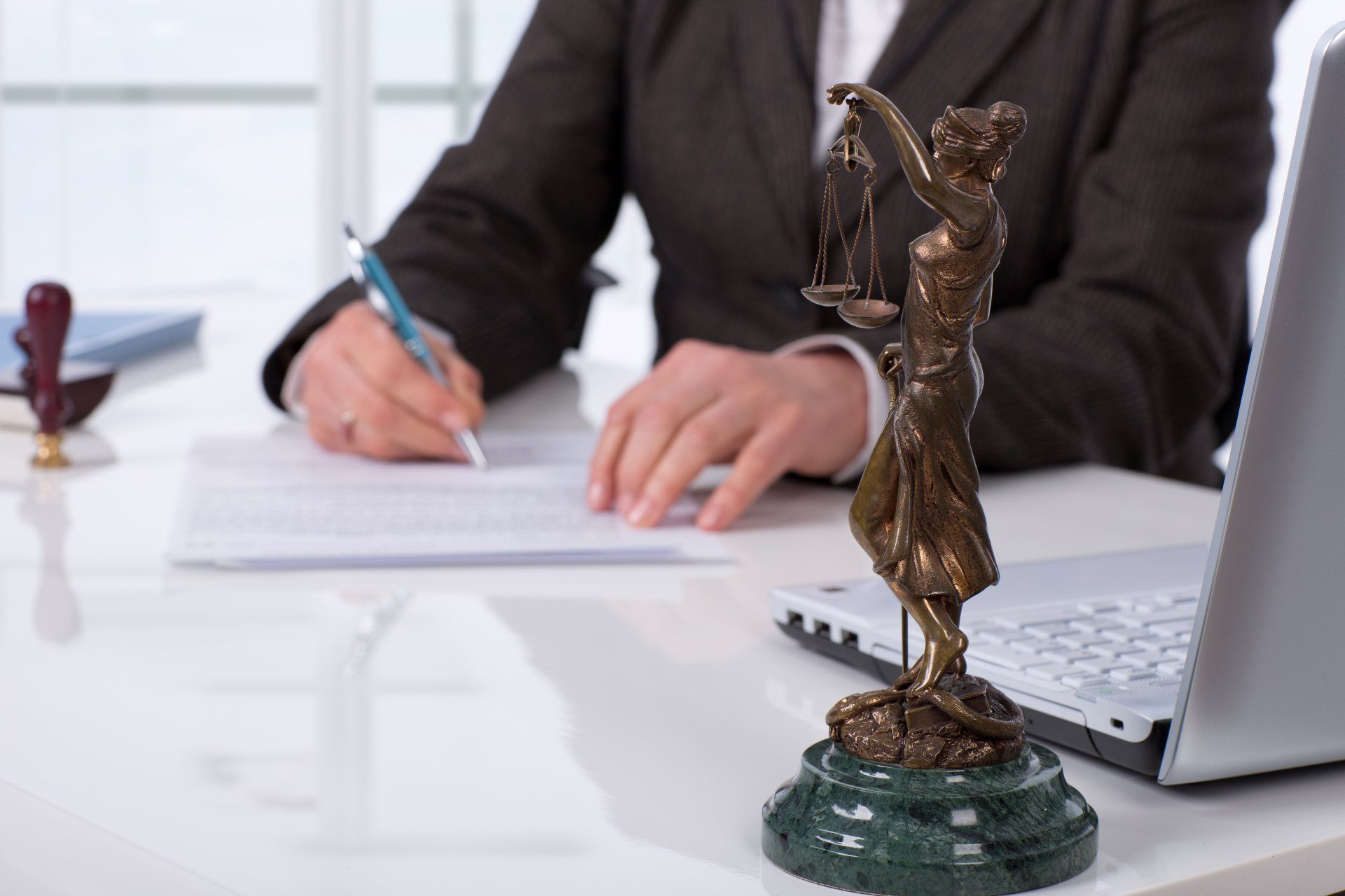 Une personne écrivant à un bureau avec une statue en bronze de la justice au premier plan