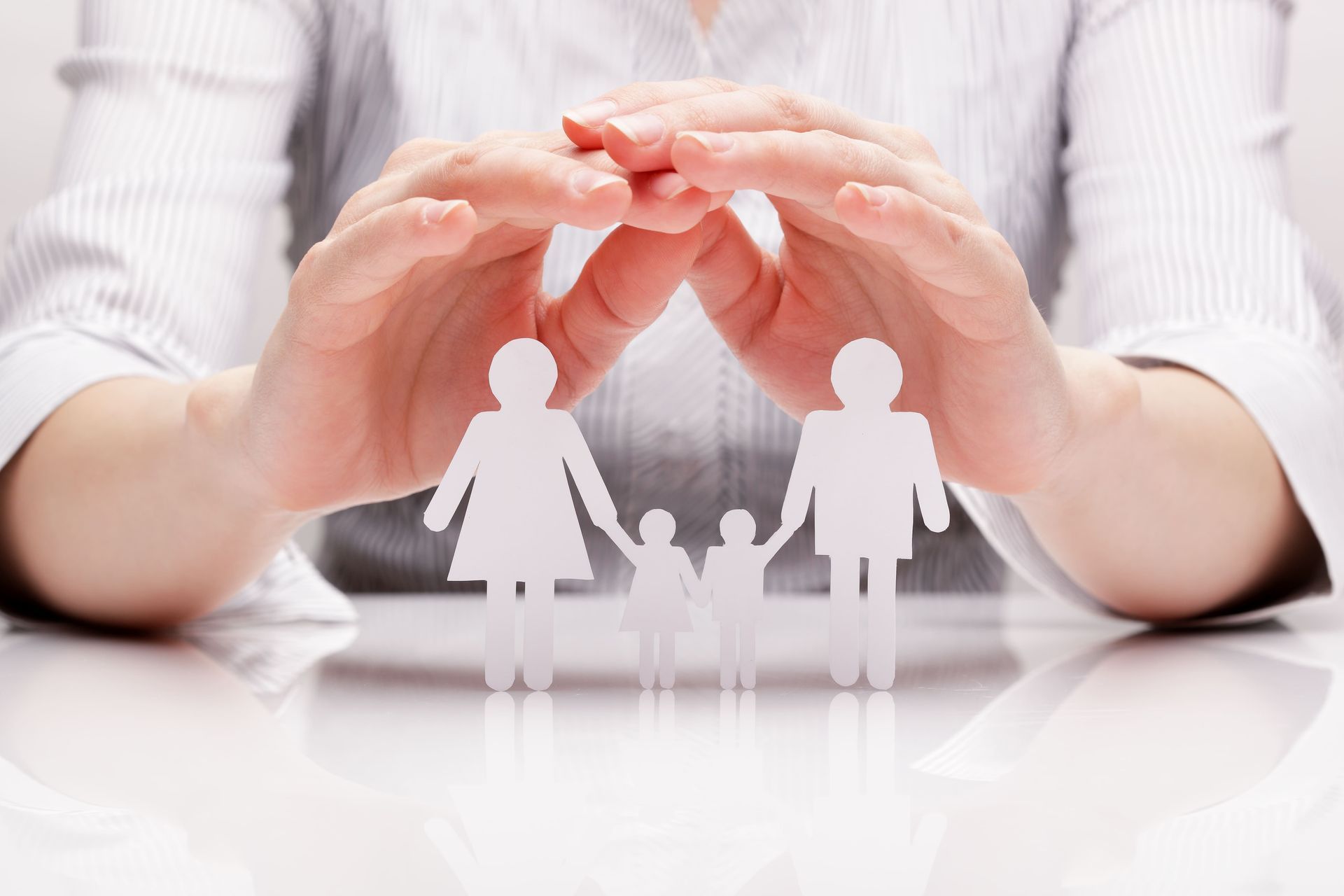 Des mains protègent des figurines familiales en papier posées sur une table, symbolisant la protection et la sécurité de la famille.