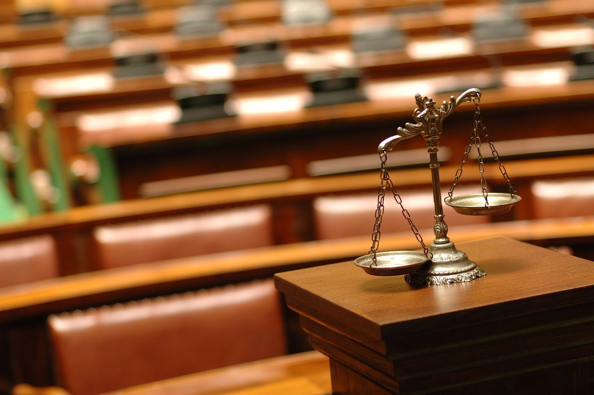 Une balance est posée sur un banc en bois dans une salle d'audience, avec des rangées de sièges vides floues en arrière-plan.