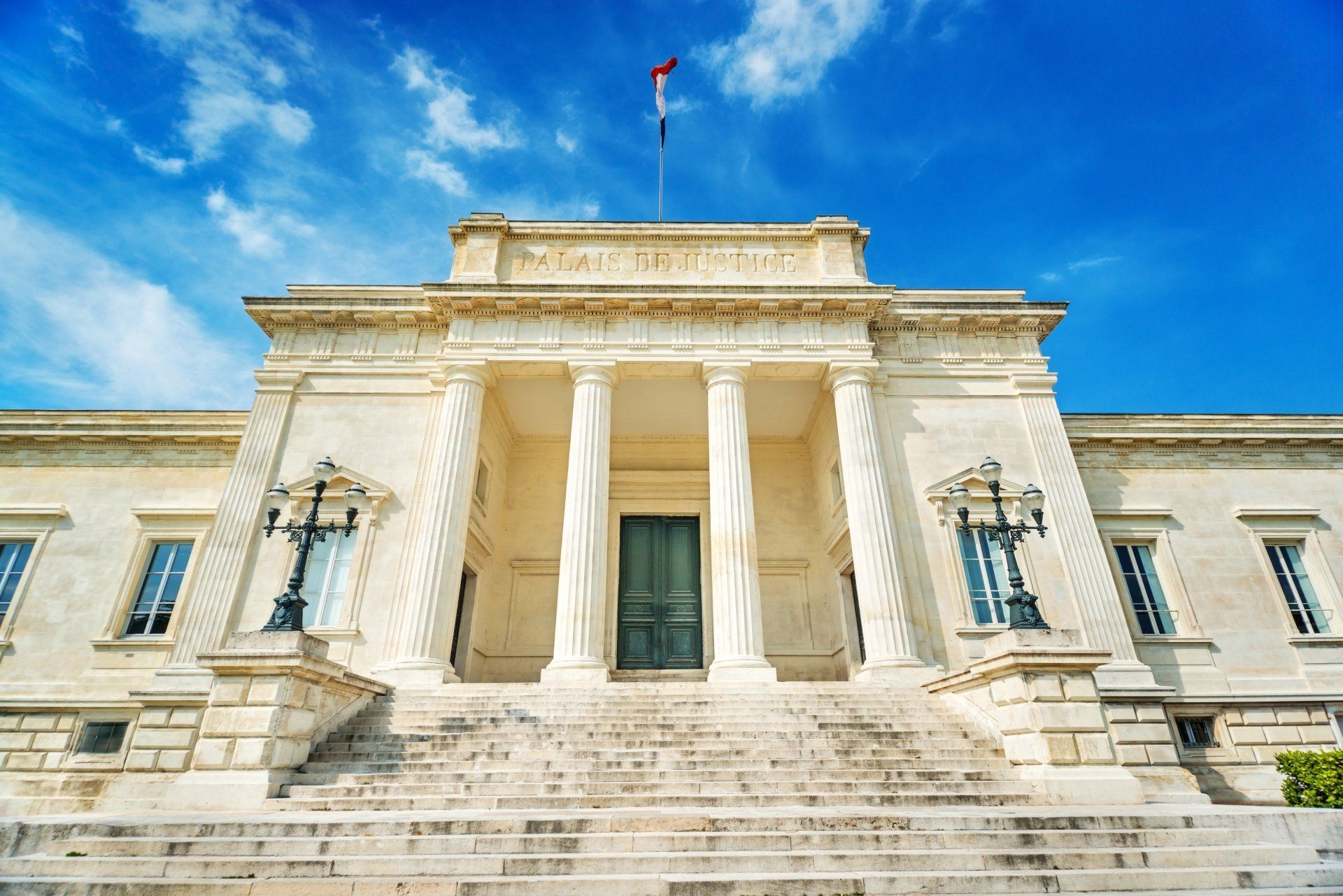 Grand bâtiment néoclassique en pierre avec colonnes et escaliers sous un ciel d'un bleu éclatant