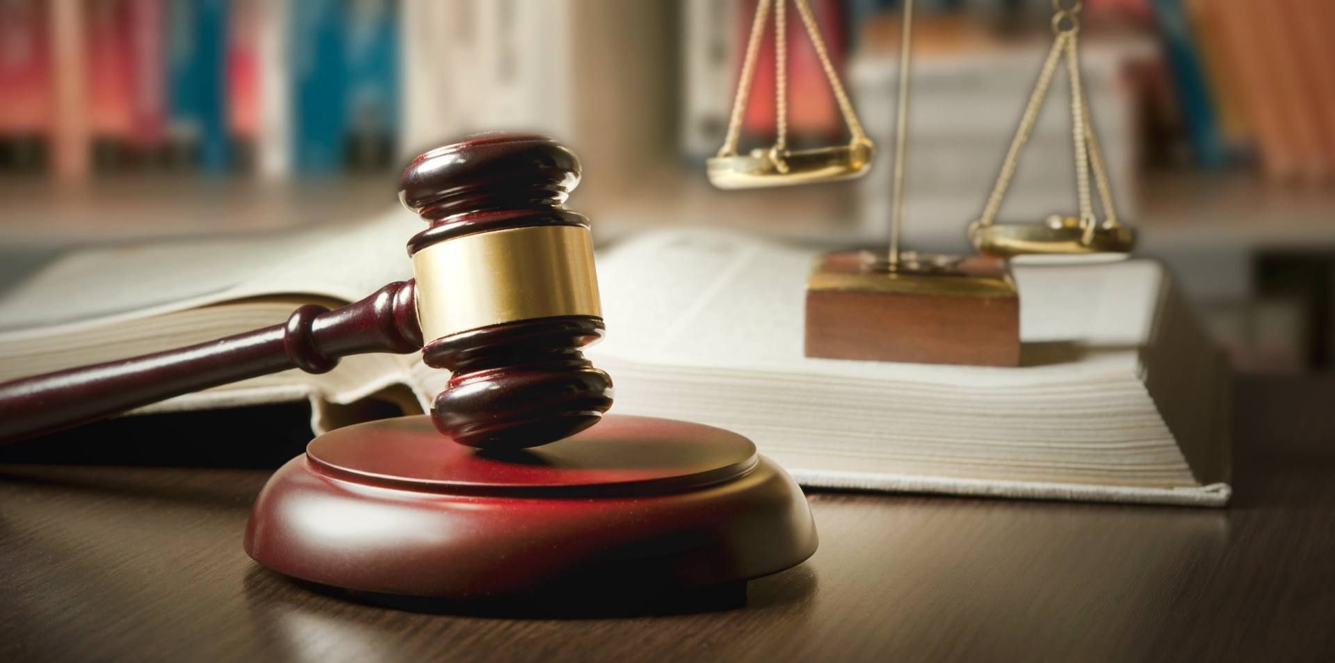 Un maillet sur un bureau, avec une balance de la justice en arrière-plan, symbolisant la loi et le jugement.