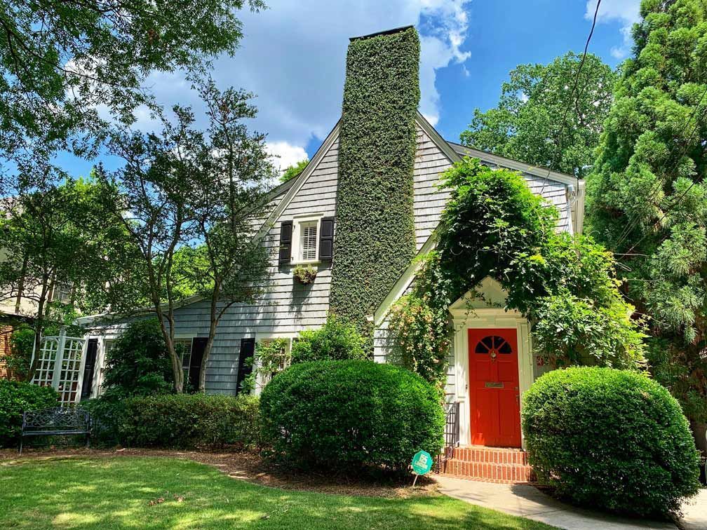 Charmant cottage recouvert de lierre, avec une porte d'entrée rouge vif, une cheminée en pierre et un jardin luxuriant.