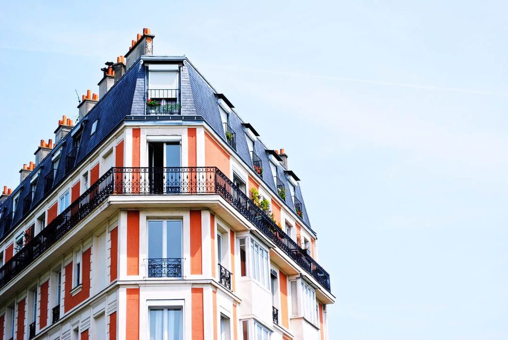 Angle d'un immeuble parisien blanc et orange avec balcons se détachant sur un ciel bleu