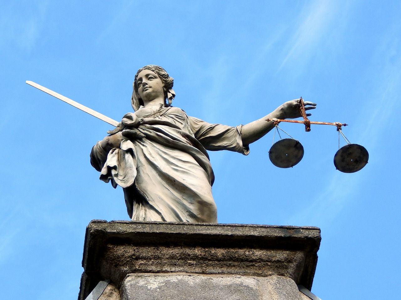Statue de la Justice tenant une balance et une épée sur fond de ciel bleu