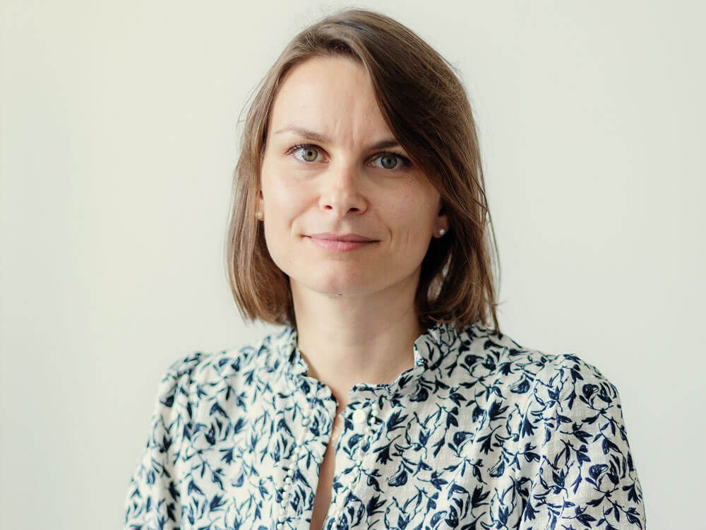 Portrait d'une femme en chemisier à motifs sur fond clair, regardant l'objectif avec un léger sourire