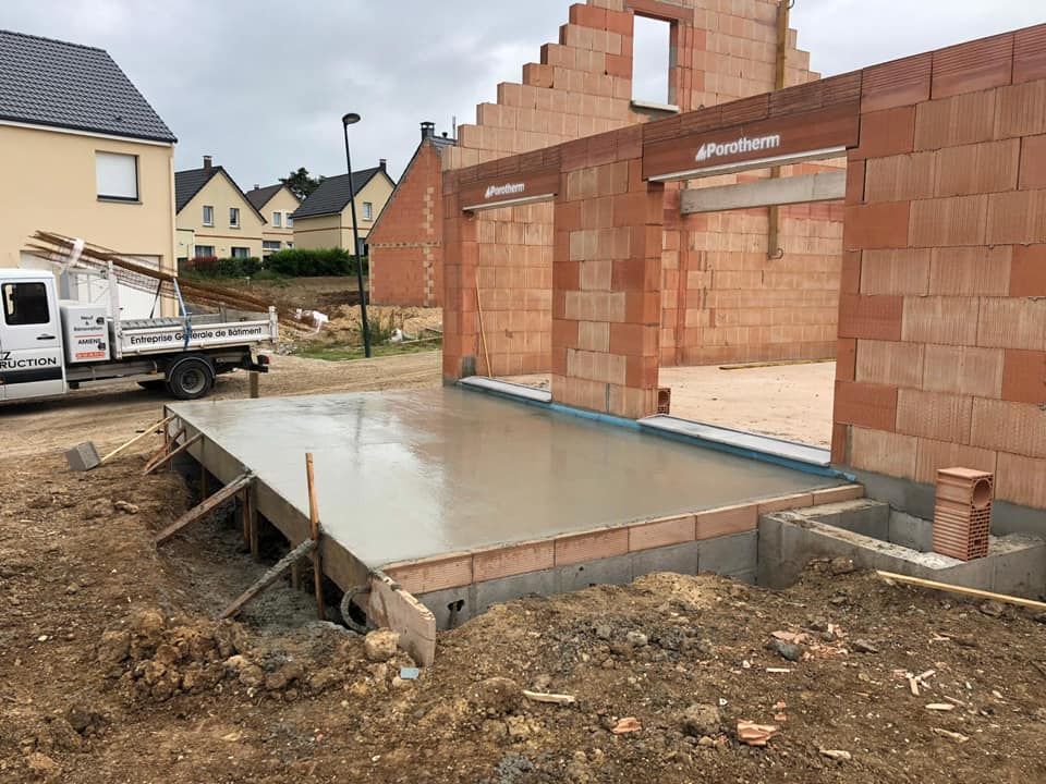 Dalle de fondation en béton à côté d'une maison en briques inachevée en construction