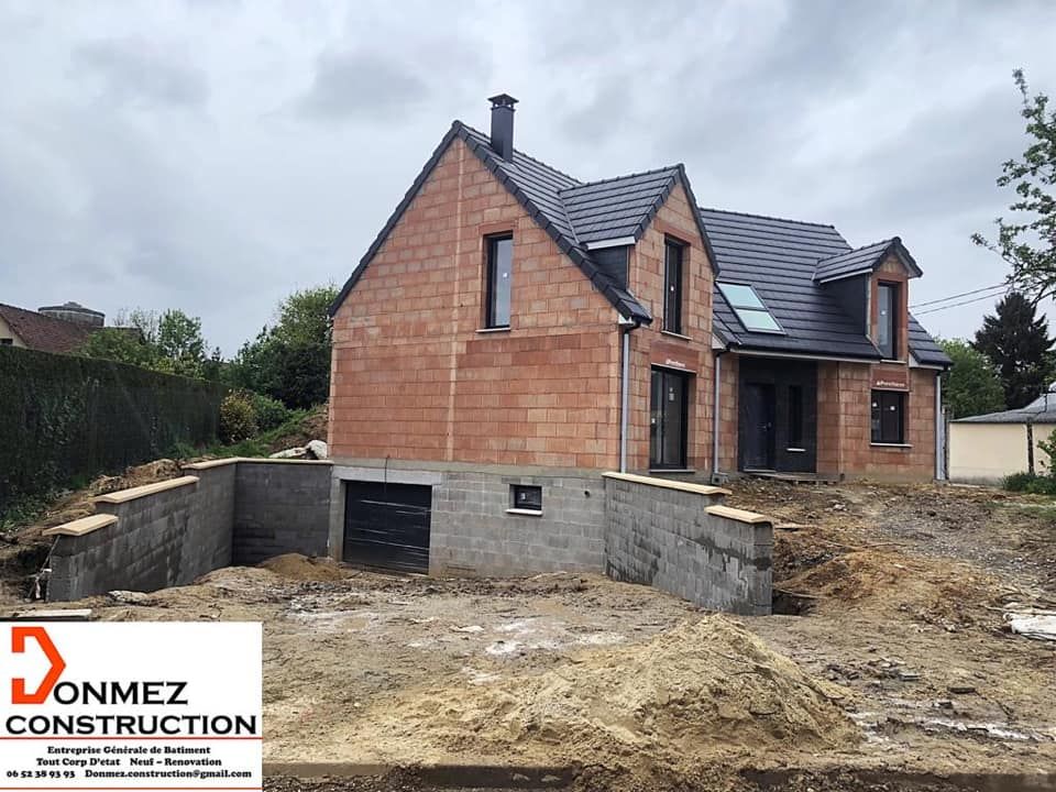 Maison en briques en construction, fondations inachevées et terrain boueux sous un ciel nuageux